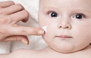 Mano de un adulto aplicando crema en la cara de un bebé.